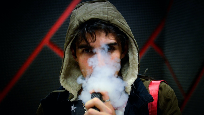 young man with brown hair wearing hooded jacket while using vape