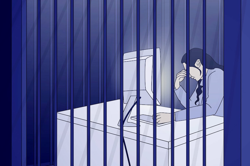 A person sits at a computer desk behind bars, their head resting on one hand, lit up by the screen 