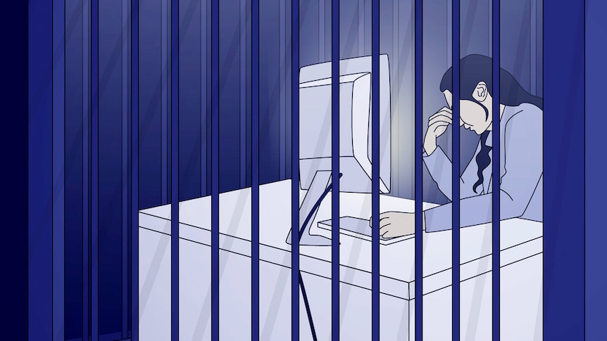 A person sits at a computer desk behind bars, their head resting on one hand, lit up by the screen 