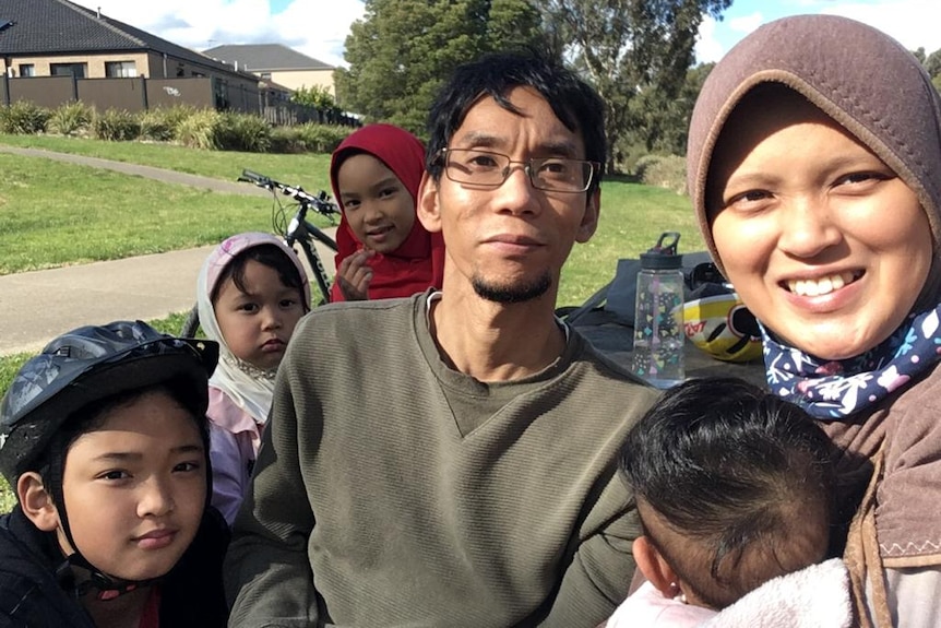 Woman in hijab smiles on right of frame, man and four children by side.