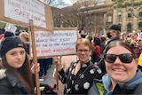 Three women hold signs and stare at camera at a Melbourne rally against the Roe v Wade decision