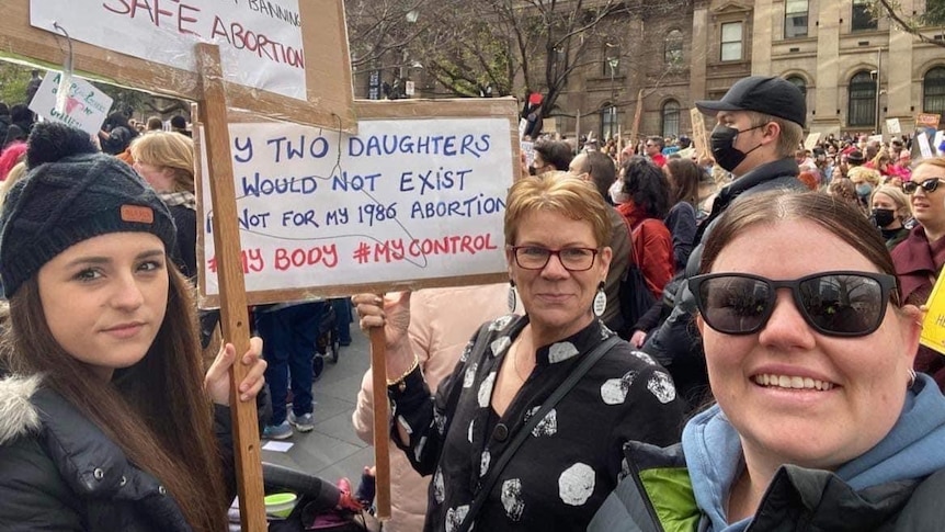 Three women hold signs and stare at camera at a Melbourne rally against the Roe v Wade decision