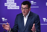 Daniel Andrews at a press conference with his hands up in front of him.