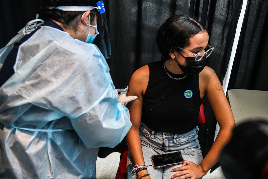 Un'infermiera in DPI completa somministra il vaccino a un bambino di 15 anni durante un evento di vaccinazione del Miami Heat il 5 agosto