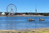 An inlet with two paddle boats and a Ferris wheel and carnival attractions in the background.