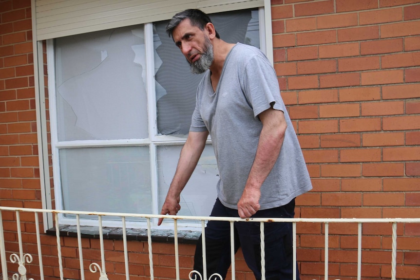 The father of two brothers charged for planning a terror act points to a broken window shutter in front of a broken window.