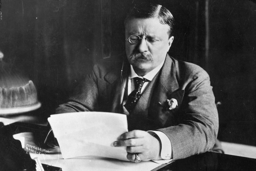 a man sits behind a desk reading through papers. Black and white image