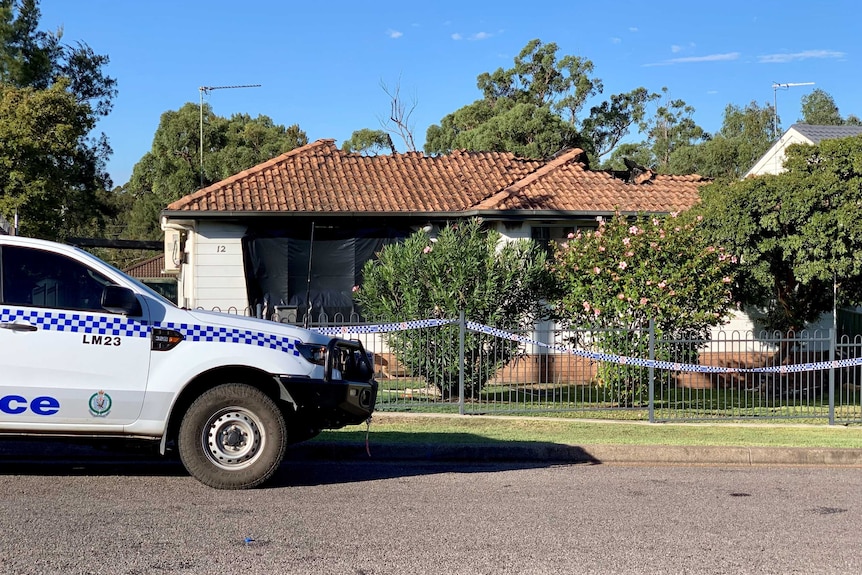 A police car parked out the front of a fire-damaged weatherboard home, with part of the roof missing.