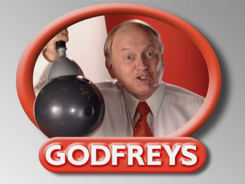 A man with a white shirt and red collar lifts a bowling ball with a vaccum. He's in a red circle with Godfreys underneath.
