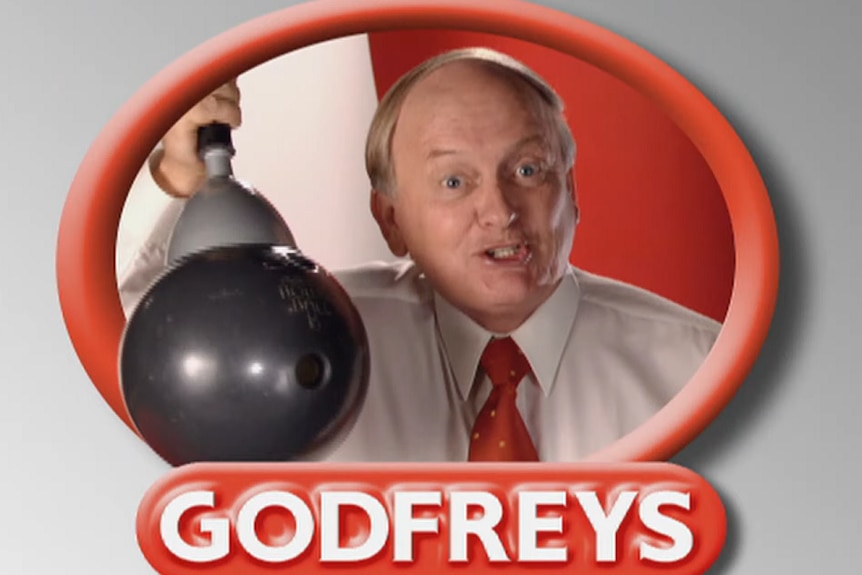 A man with a white shirt and red collar lifts a bowling ball with a vaccum. He's in a red circle with Godfreys underneath.