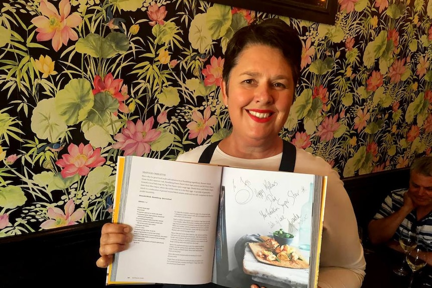 Bundaberg chef Amanda Hinds holding a copy of the Australia Cooks cookbook.