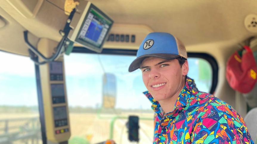 A teenage boy wearing a bright shirt and hat is driving a harvester