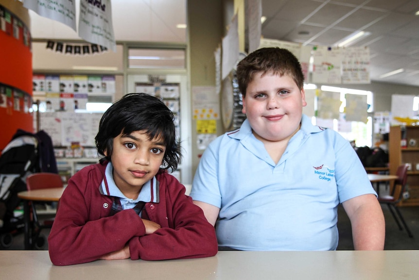 Year Two students, Hasaru and Aiden sit at a classroom desk wearing school uniforms.