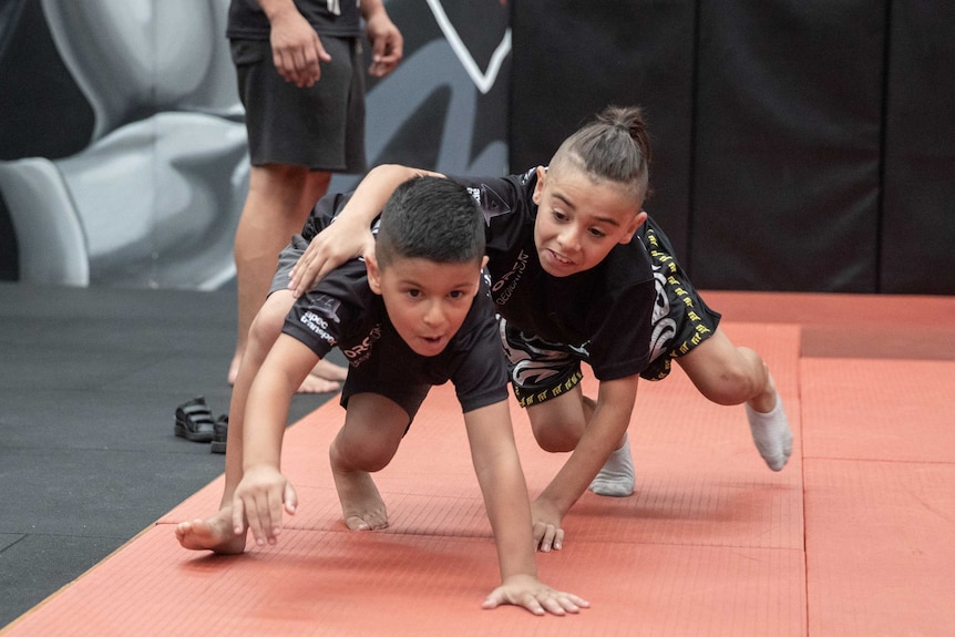 One young boy tackles another boy onto a mat.