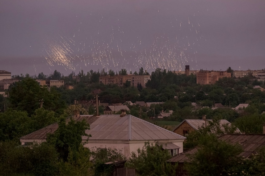 Sparks and yellow light seen raining down with homes in foreground. 