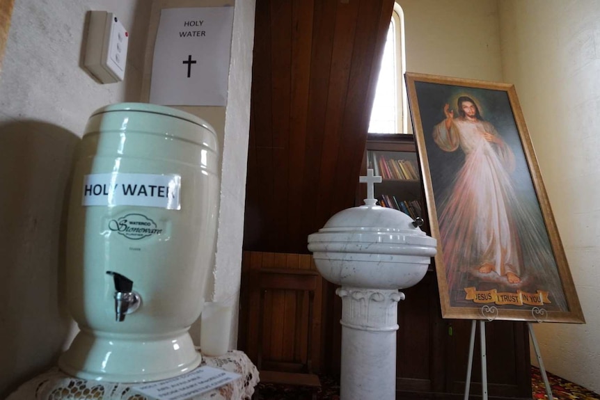 A water dispenser labelled "Holy Water" sits near a painting of Jesus