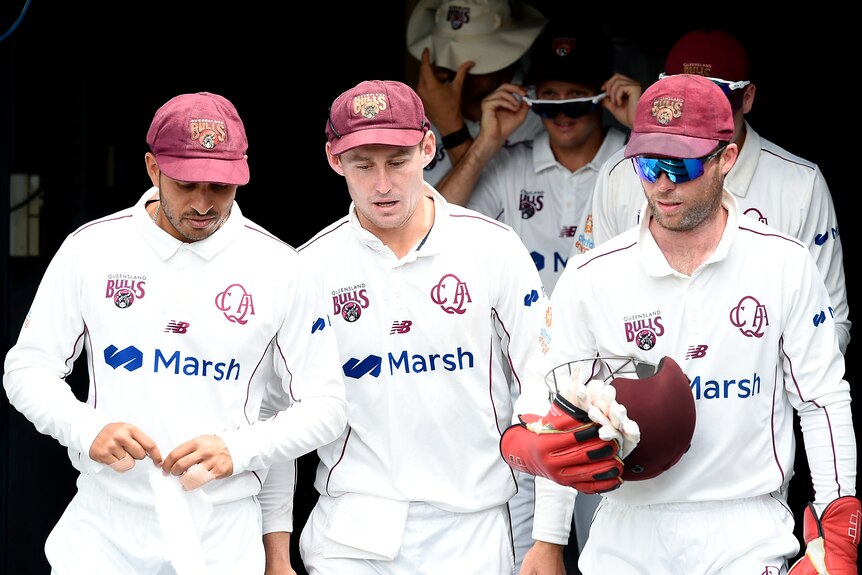Queensland players Usman Khawaja, Marnus Labuschagne and Jimmy Peirson, carrying a helmet, walk out for a Sheffield Shield game.