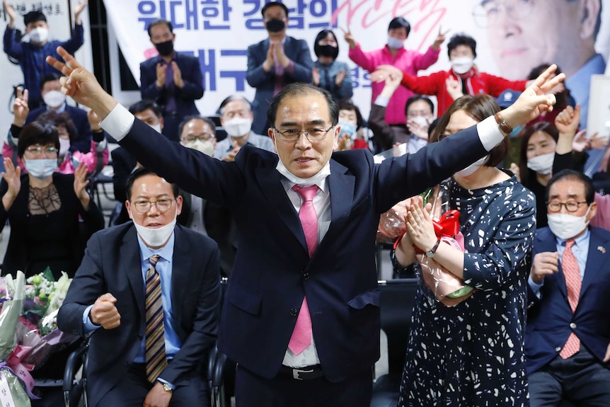 People wearing masks celebrate in front of political posters.