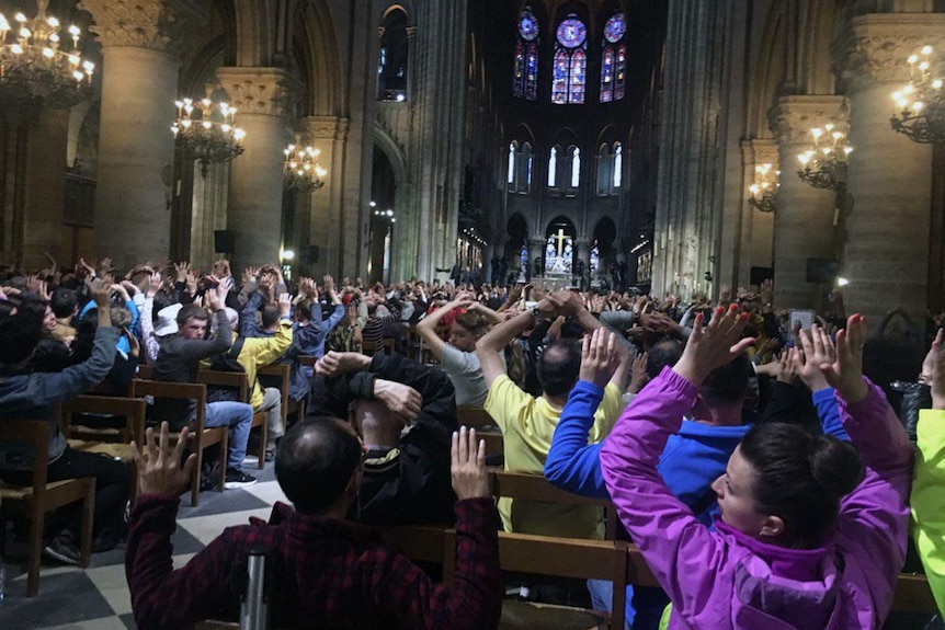People sit inside the Notre Dame cathedral with their hands in the air.