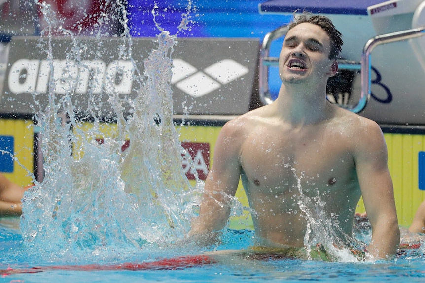 Hungary's Kristof Milak thrashes his fists into the water in front of a yellow pool wall and pool block.