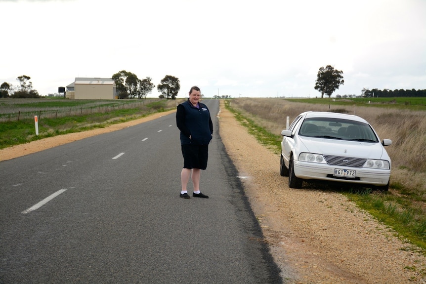 Nurse Bridget McKenzie stands by a stretch of rural road with a car in the background.