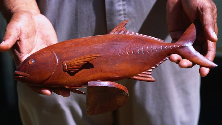 A man holding a wooden carving of a fish