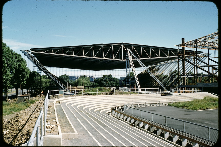 A winged building under construction, next to a running track