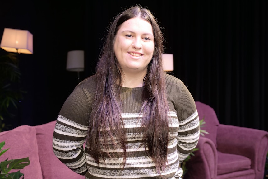 Charlotte Lee stands smiling at the camera wearing a white and dark grey jumper.