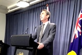 Peter Collier WA Education Minister speaking at a podium with WA flag behind.