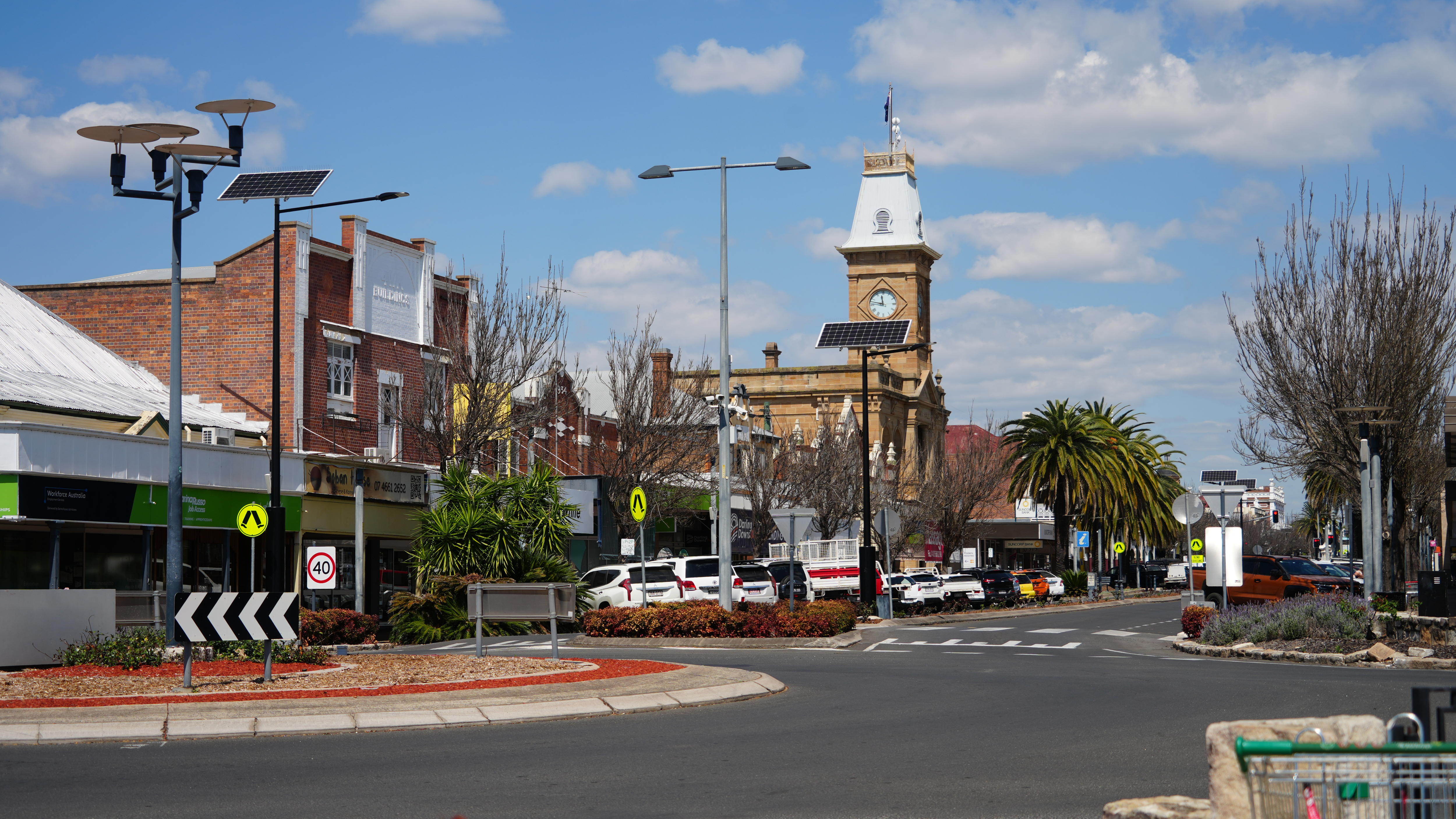Wide photo of a town with a roundabout in the foreground and a clock tower in the background.