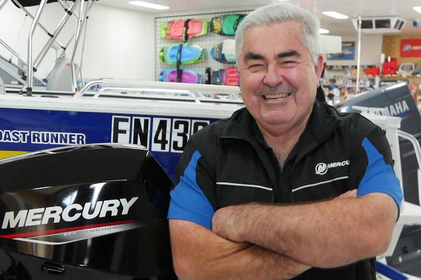 a man stands with his arms folded in a boat showroom