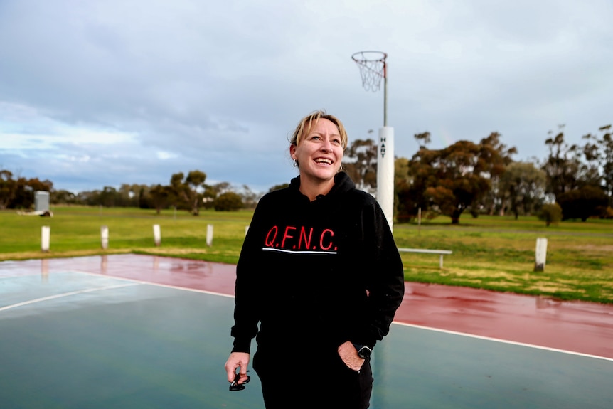 Woman wearing black jumper standing on netball court with grey skies behind