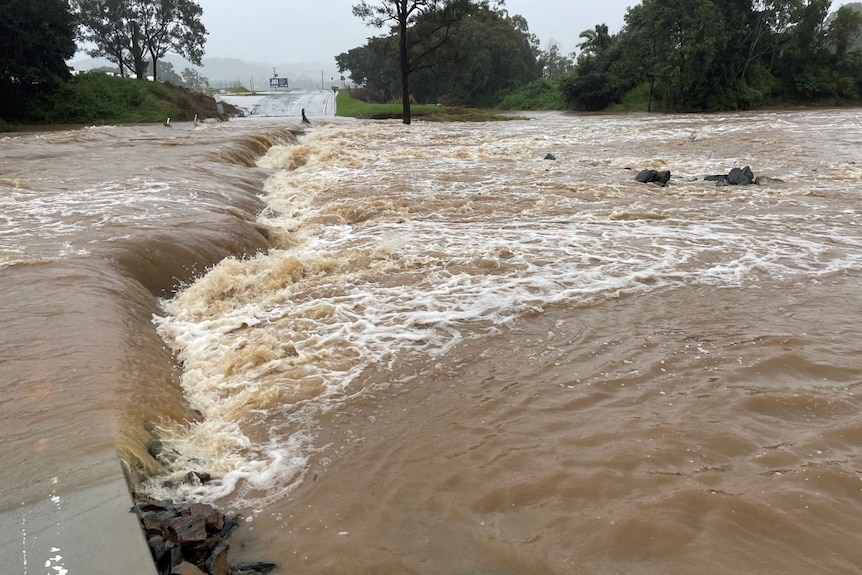 Floodwater rushes over a road.