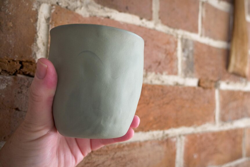 A hand holding a terracotta wine cup in front of a wall.