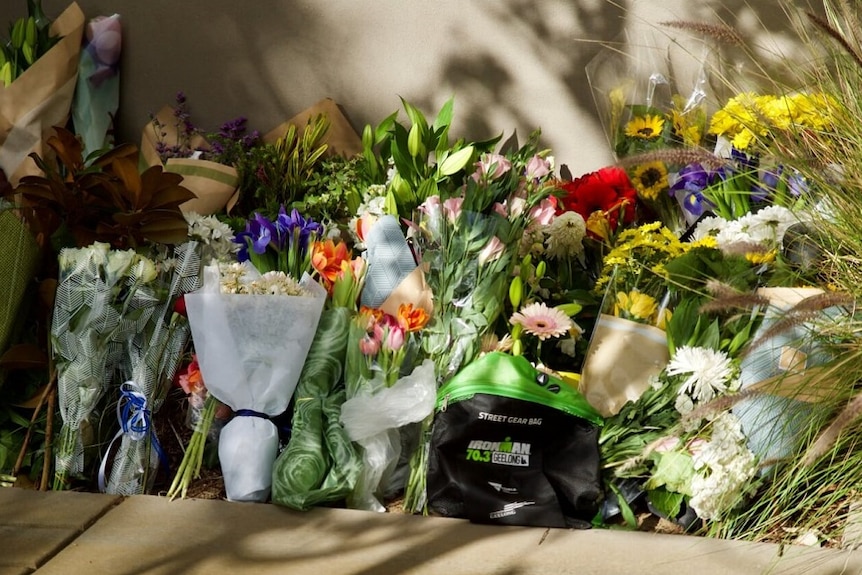 A row of bouquets of flowers is lined up against the outside wall of the Boroondara Police Station.