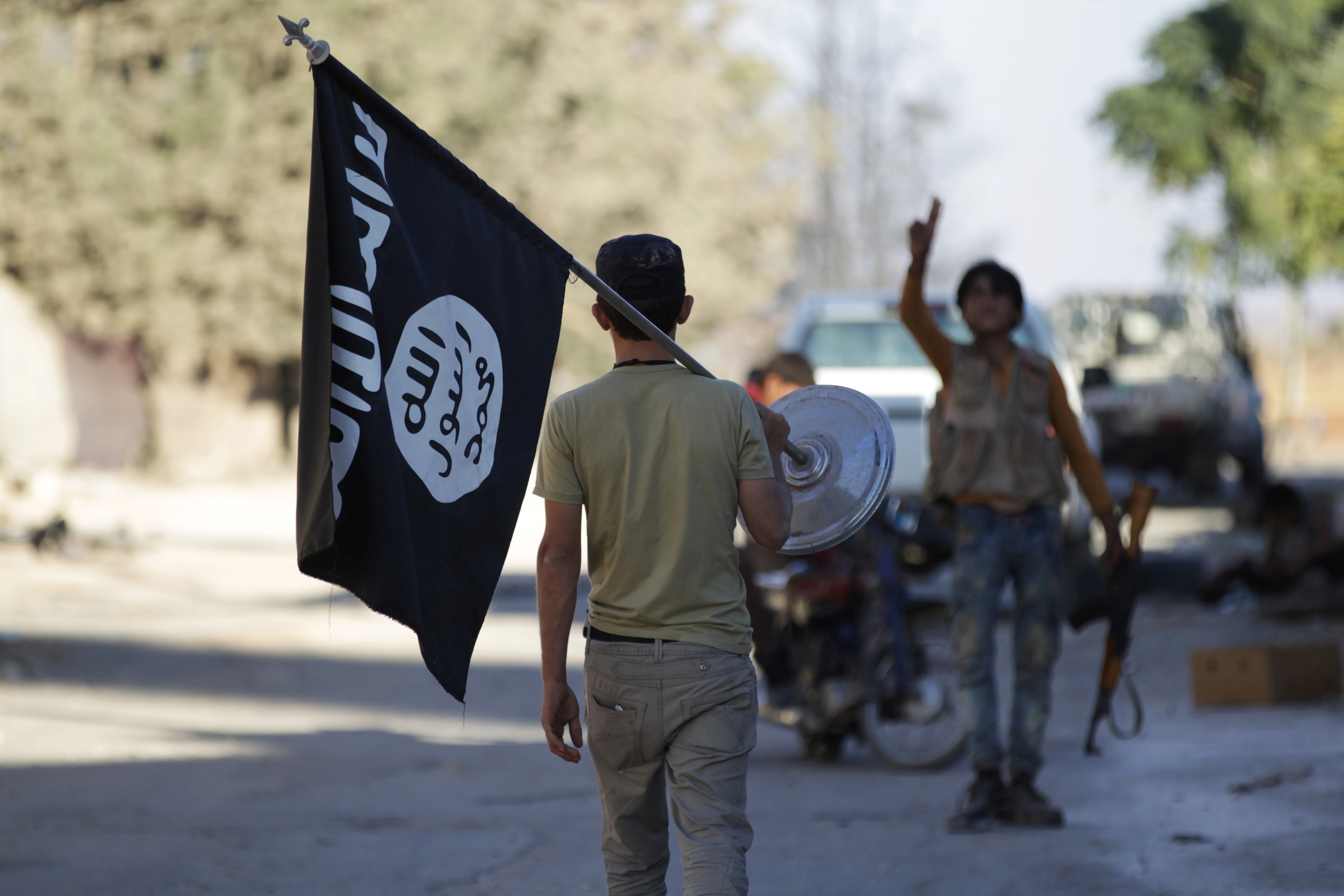 A man carries an Islamic State flag while walking towards a man carrying a rifle.