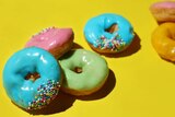 A stack of brightly coloured ice doughnuts with hundreds and thousands sit on a coloured background, a nostalgic sugar fix.