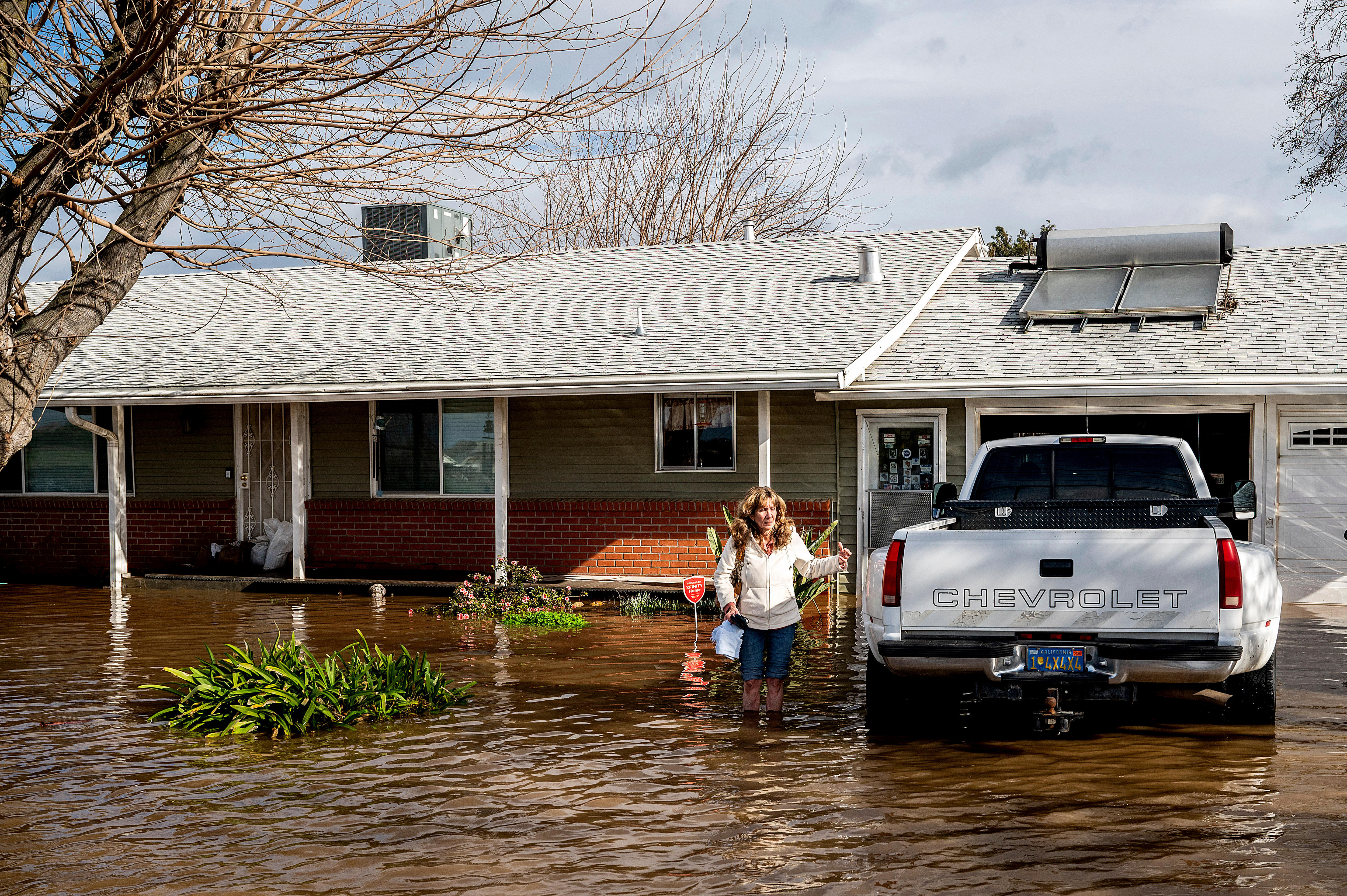 A woman up to her knees in flood water next to a car outside a house