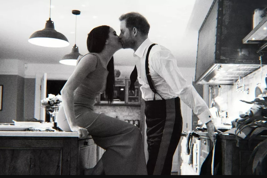 A black and white photo of Meghan sitting on a kitchen counter kissing Harry