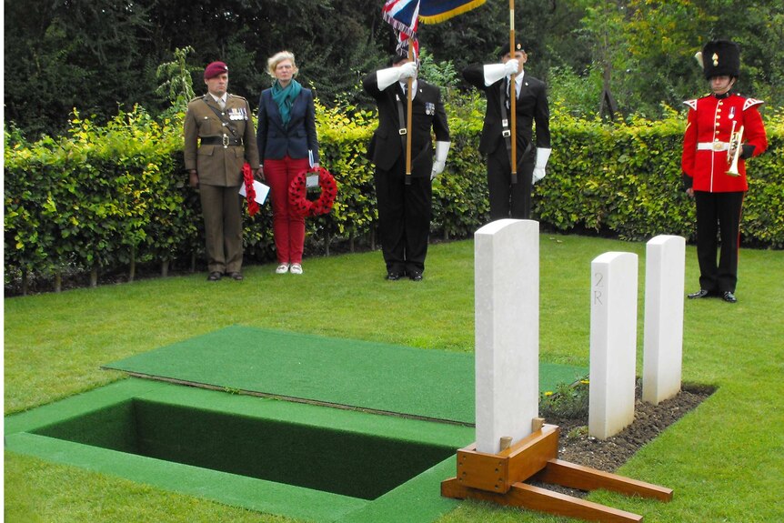 People in military uniform stand before an open grave