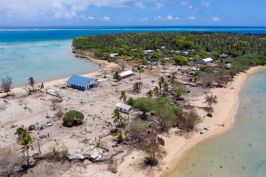 An aerial shot shows destroyed houses and buildings on a small strip of island in Tonga.