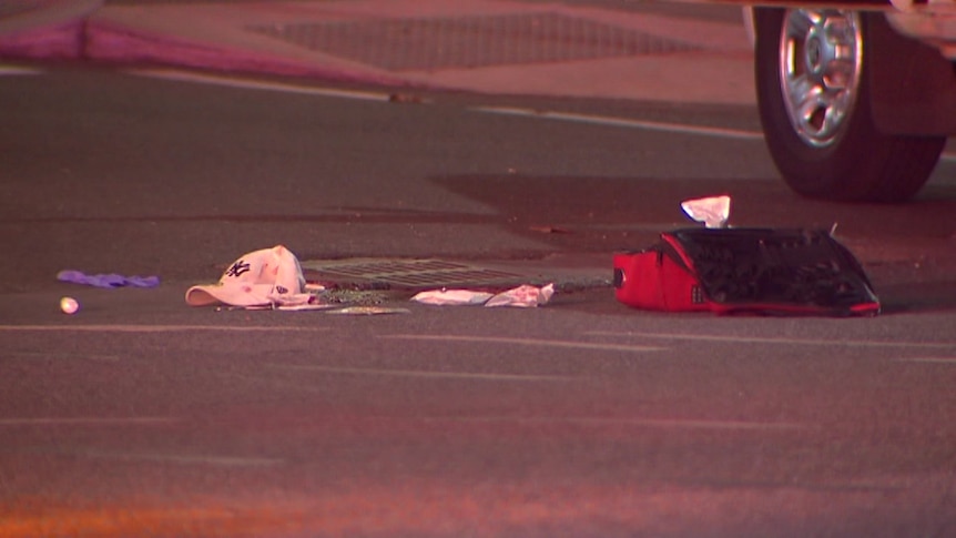 A hat, clothes and a red bag on a road next to a car wheel