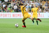 Sam Kerr runs with her arms outstretched as she prepares to kick a ball.