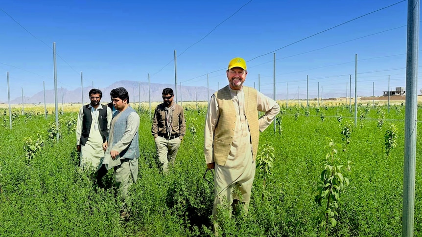 An Australian man standing in a field with Afghan farmers and blue sky above.