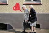 Two elderly women walk by a love heart graffitied on a wall.
