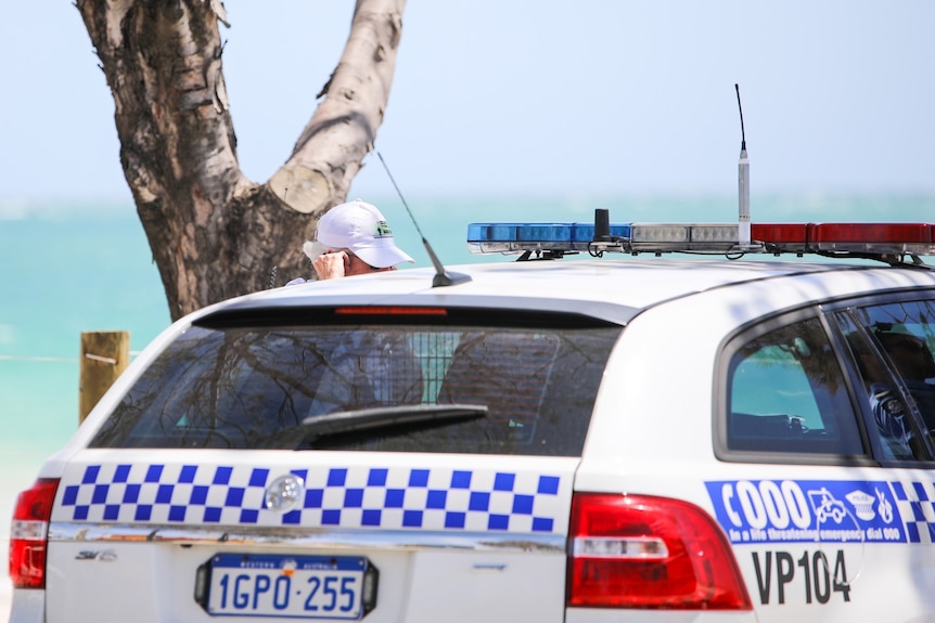 A woman speaks on a mobile phone next to a police car at Port Beach.