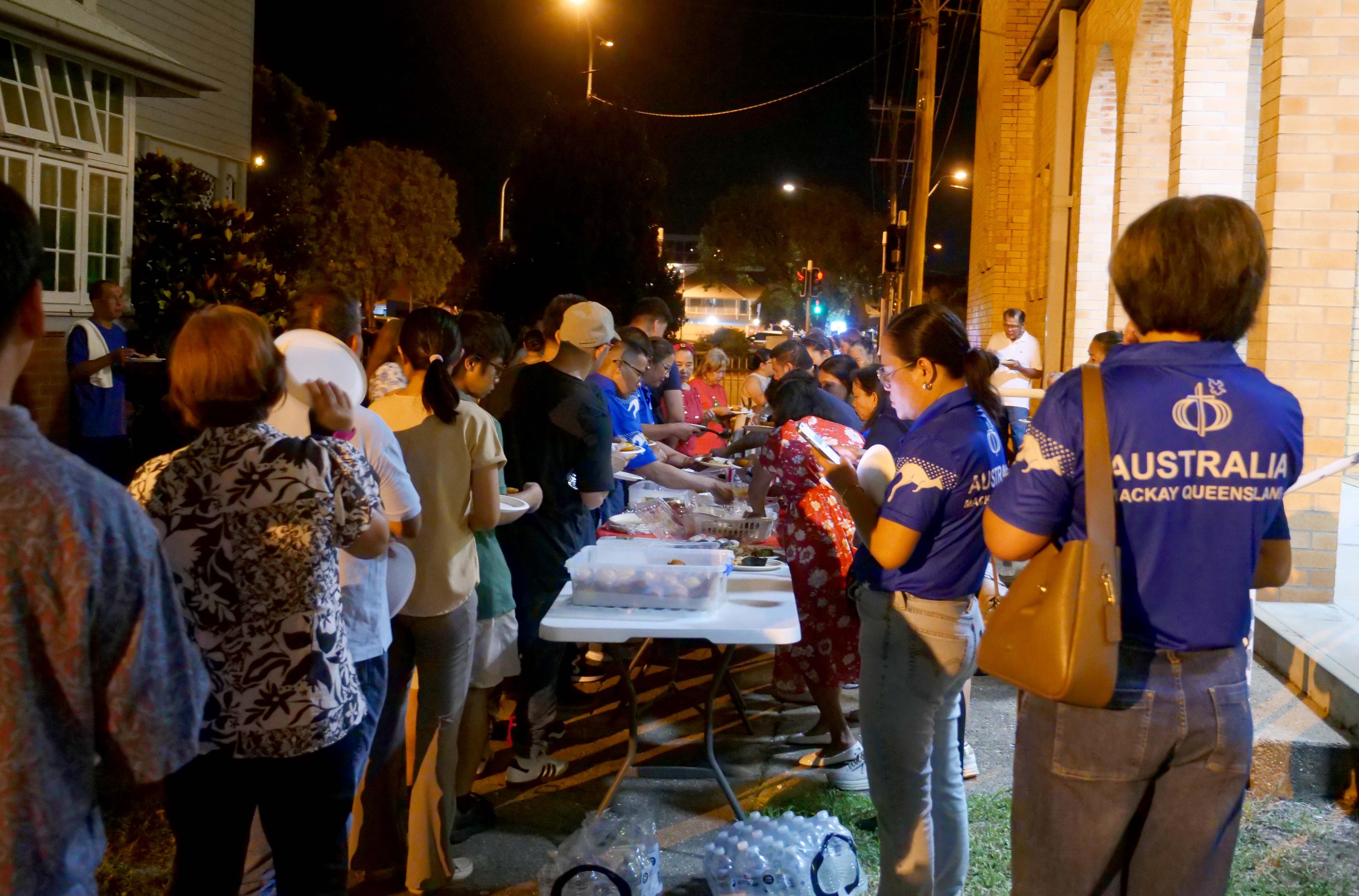 Uma multidão reúne comida em uma mesa em frente à Igreja de São Patrício para um banquete em Simbang Gabi.
