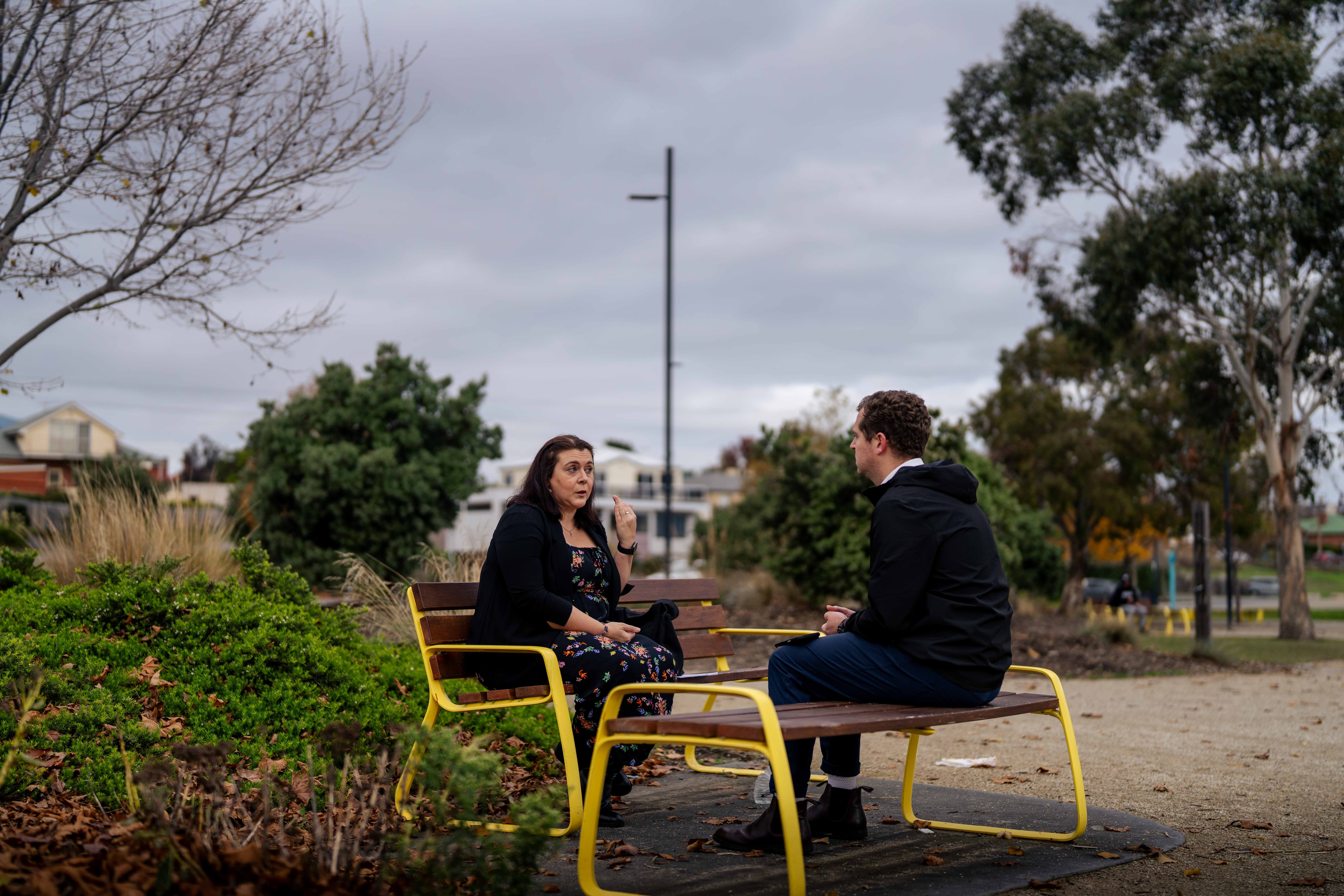 Woman sits on a park bench on a cloudy day, serious expression