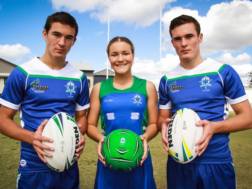 Three teenagers wearing sports uniforms on a sporting field.