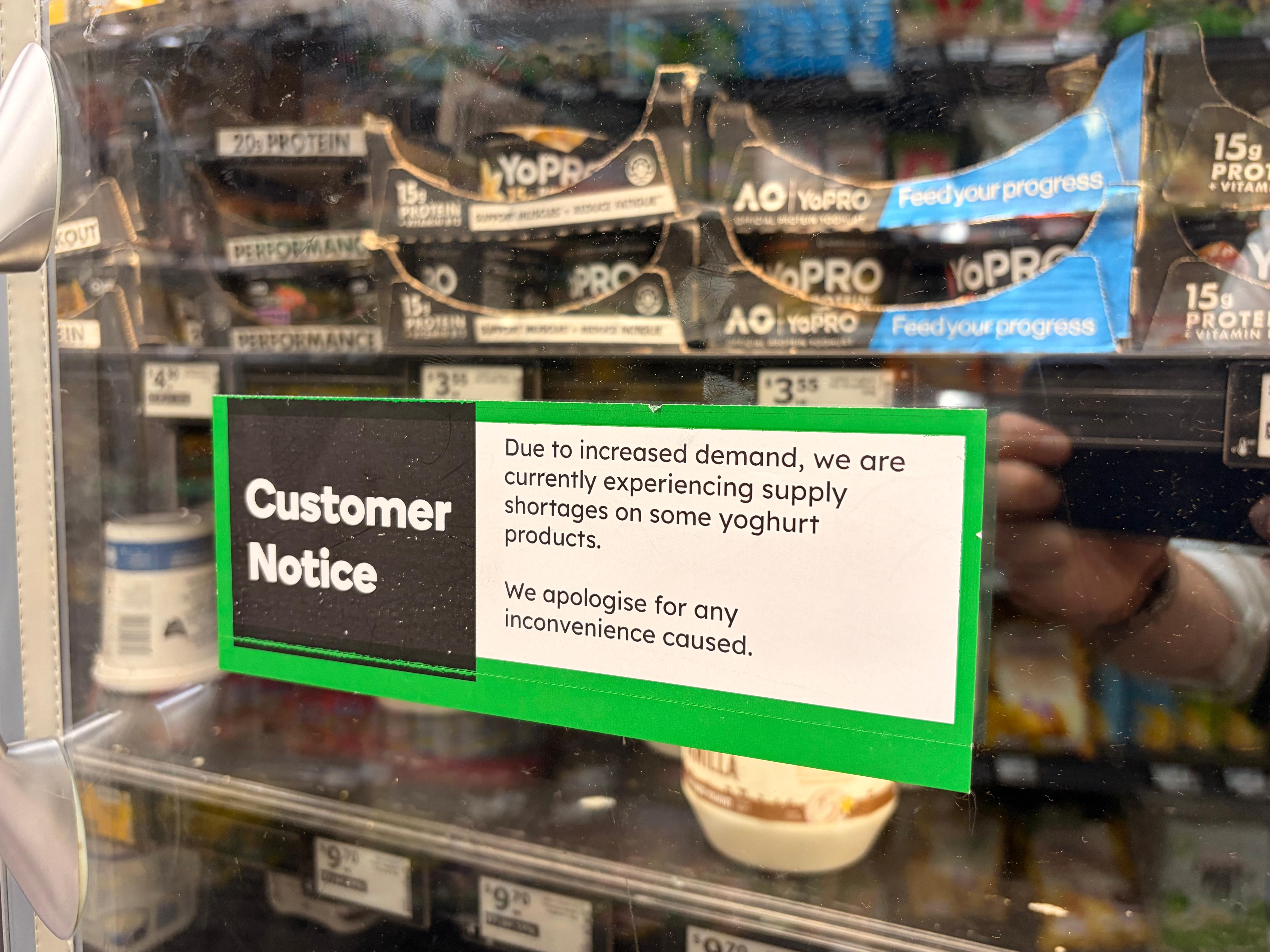 A customer notice sign with a green border in front of a yoghurt aisle.